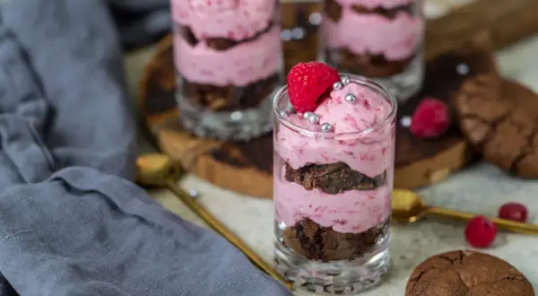 Ljuvlig hallonmousse till tårta i glas, varvad med chokladkaka och toppad med färsk hallon och silverkulor.