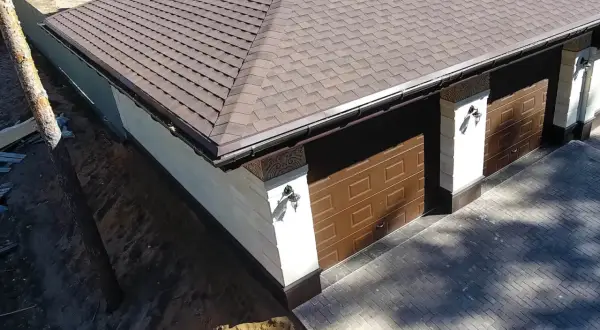 Nowy dach z gontu pokrywa budynek z dwoma brązowymi bramami garażowymi.