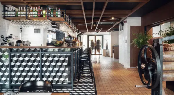 Nowoczesny bar w hotelu Almond. Geometryczne wzory na ladzie i podłodze, drewniany sufit, butelki alkoholi na półkach.