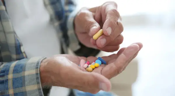 Dłoń starszego mężczyzny trzyma garść kolorowych tabletek, jedną żółtą kapsułkę, być może inhibitory MAO.