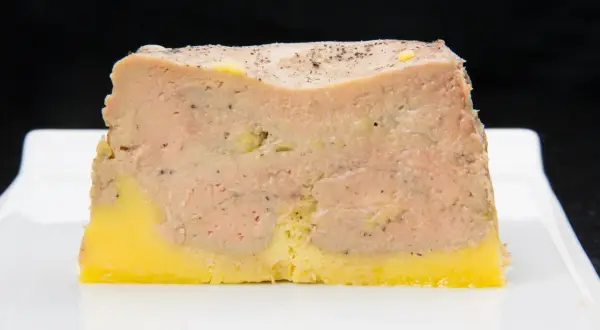 Tranche de pâté en croûte, avec une couche de viande rose et une base jaune, prête pour la cuisson.