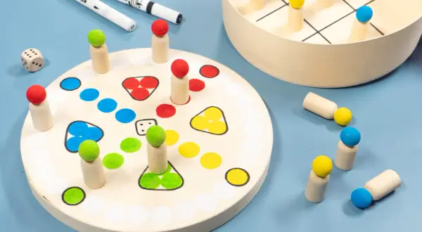 Holzfiguren und Würfel für selbst gebastelte Spiele. Ein Spielbrett mit bunten Feldern und ein Tic-Tac-Toe-Spiel laden zum Spielen ein.
