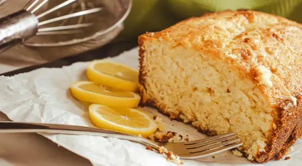 Puszysta babka bez jajek, pachnąca cytryną, czeka na widelca. Obok plastry cytryny i metalowa trzepaczka.