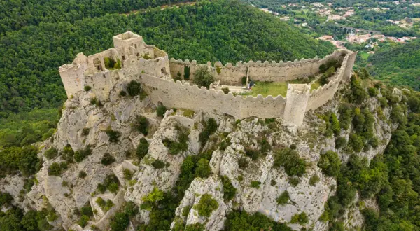 Vestiges d'un château abandonné en Occitanie, perché sur un éperon rocheux, dominant une vallée verdoyante.