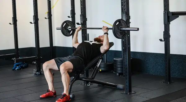 Mężczyzna z brodą wykonuje ćwiczenie incline press na ławce skośnej w siłowni.