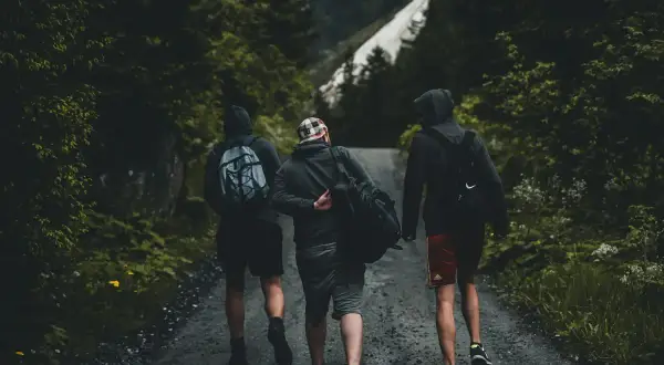 Tres amigos caminan por un sendero boscoso, una aventura perfecta para conocer gente y disfrutar de la naturaleza.