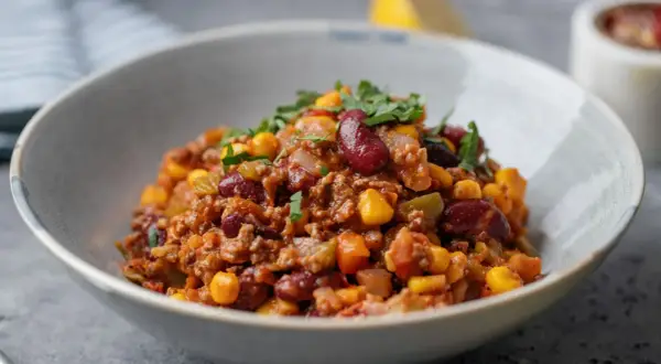 Miseczka pełna aromatycznego chili con carne z fasolą, kukurydzą i mielonym mięsem, posypana świeżą natką pietruszki.