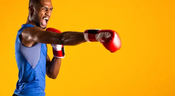 A boxer in a blue tank top throws a punch, his face contorted in a roar. He's ready to compete in the junior welterweight weight class.