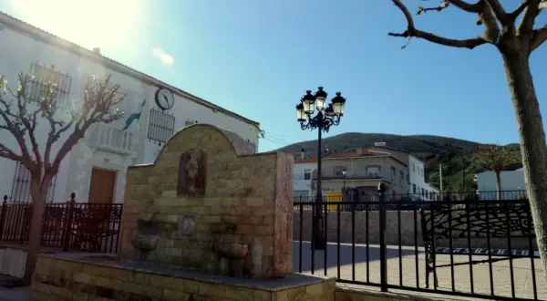 Fuente de piedra en Chercos, Almería, con un edificio blanco y un reloj al fondo.