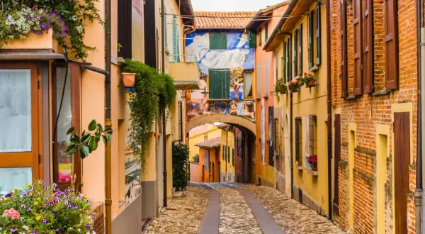 Un vicolo pittoresco tra i borghi medievali dell'Emilia Romagna, con case colorate, fiori e murales vivaci.