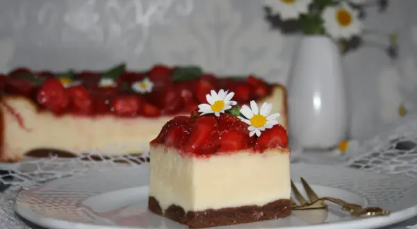 Pyszny sernik z truskawkami, udekorowany świeżymi kwiatkami, kusi swoim wyglądem.