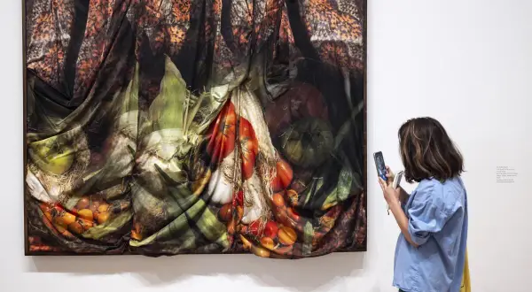 A woman photographs a draped artwork featuring fruits and vegetables, made in LA Hammer.