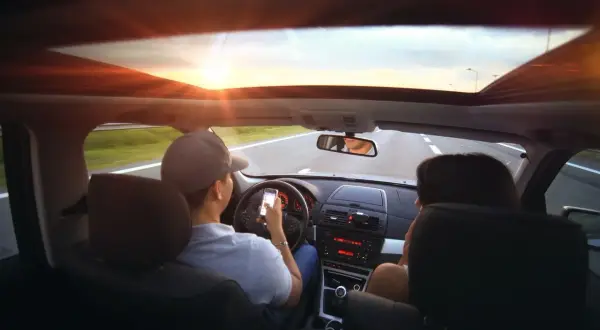 Kierowca z telefonem w ręku, zasada ograniczonego zaufania w praktyce. Słońce zachodzi, droga przed nimi.