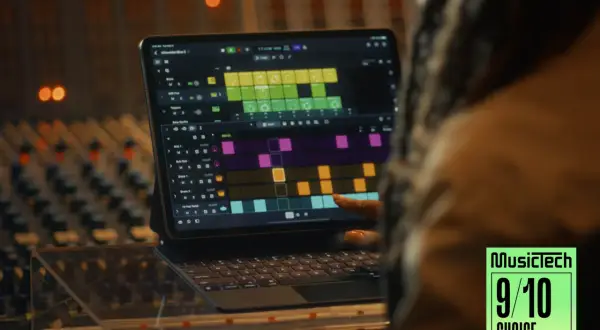 A person's finger touches a tablet displaying Logic Pro for iPad, showing a colorful grid of musical patterns, in a recording studio.