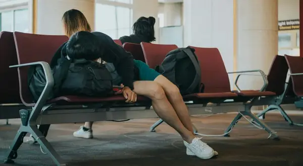 Zmęczony podróżny śpi na lotnisku, wyraźne objawy jet lag.