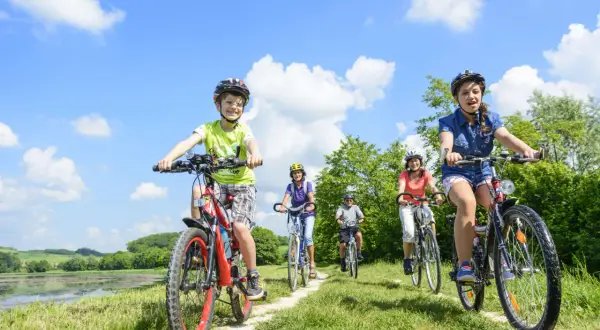 Familie genießt das **Radfahren mit Kindern** auf einem sonnigen Weg am See.