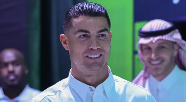 Cristiano Ronaldo w białej koszuli, uśmiecha się. W tle mężczyzna w tradycyjnym arabskim stroju.