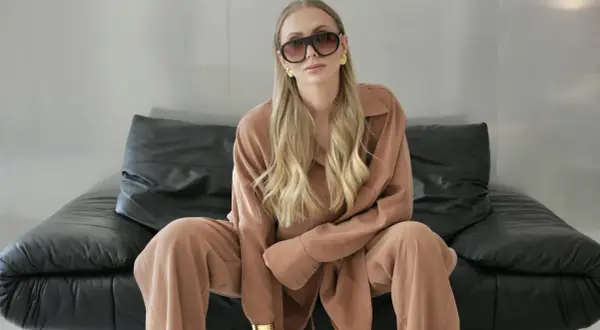 Kobieta w okularach i brązowym komplecie, idealnym do stylu biznes casual, siedzi na czarnej skórzanej kanapie.