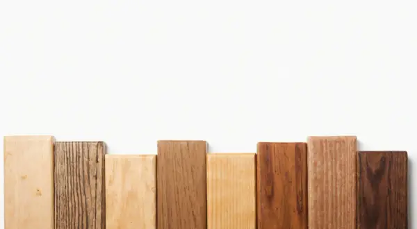 Bloques de madera dura de diferentes tonos y texturas, dispuestos en fila sobre fondo blanco.