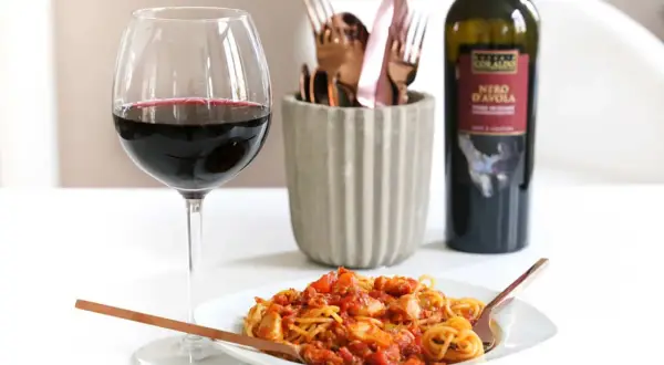 Ein Glas Rotwein und eine Portion Spaghetti Bolognese mit einem Hauch von Rotwein. Perfekt für einen gemütlichen Abend.