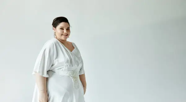 Uśmiechnięta panna młoda w pięknej, białej sukience weselnej plus size z ozdobnym pasem.