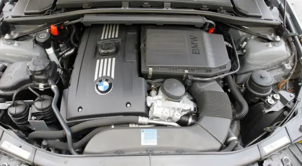 Silnik BMW E90. Widoczny jest czarny, plastikowy kolektor dolotowy, pokrywa silnika z logo BMW i oznaczeniem M, a także zbiornik płynu chłodniczego.