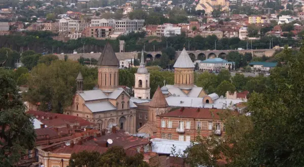 Widok na Tbilisi, gdzie zabytkowe cerkwie i domy z czerwonymi dachami opowiadają historię Gruzji. W tle widać wzgórza i nowoczesne budynki.