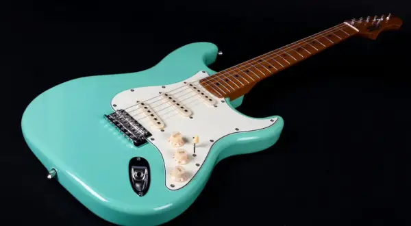 Turkusowa gitara elektryczna, idealna do nauki jak grać na gitarze elektrycznej. Ma biały pickguard i drewnianą podstrunnicę.
