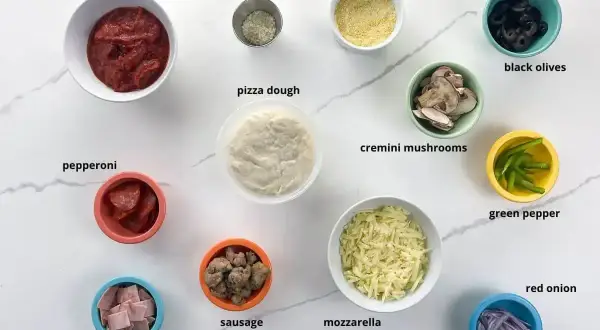 Składniki na pizzę: sos, ciasto, ser, pepperoni, szynka, kiełbasa, pieczarki, oliwki, papryka, cebula, parmezan, mąka kukurydziana.