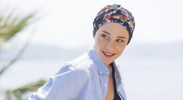 Frauen mit einem gebundenen Kopftuch, das sie während der Chemo tragen, lächeln zuversichtlich in die Kamera.