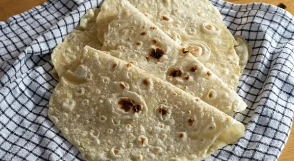 Świeżo upieczone placki na tortilla przepis, ułożone na kratkowanej ściereczce. Idealne do wrapów i quesadilli.
