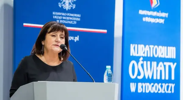 Kobieta przemawia przy mównicy. Dowiadujemy się, jak napisać wniosek o nagrodę kuratora oświaty.