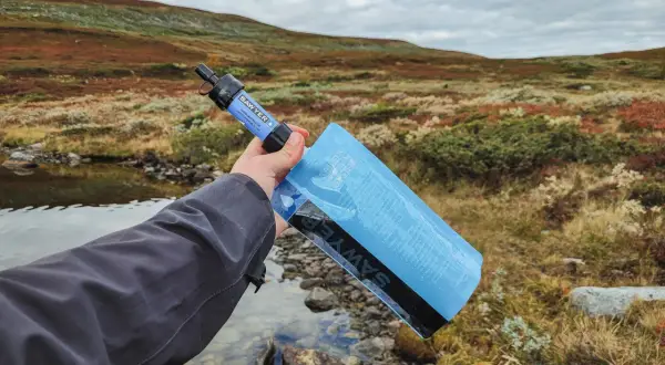 Vattenrening vandring: en hand håller en Sawyer vattenfilterpåse vid en bäck i fjällterräng.