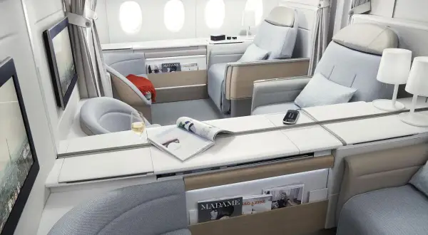 Luxuriöse Sitze in der **first class** eines Flugzeugs, mit Magazinen, einem Glas Wein und Bildschirmen.