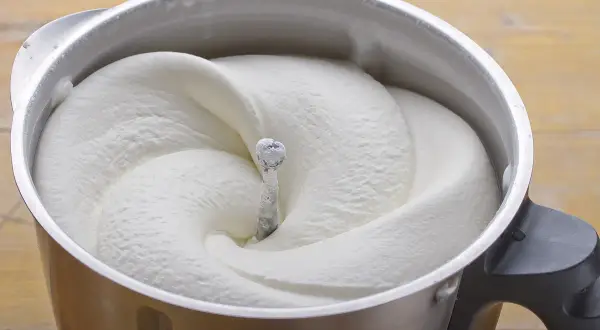 Crema de batir perfectamente montada en un bol de metal, lista para decorar postres.