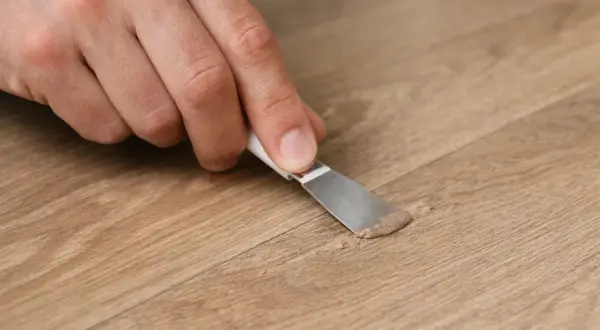 Mano che applica stucco per la riparazione parquet su una fessura del legno.