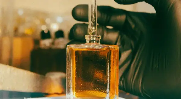 Kropla płynu, zawierającego cenną **molecule**, spada z pipety do kwadratowej buteleczki.
