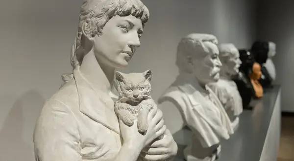 Rzeźba Camille Claudel "Plotkarki" - kobieta z kotem, obok popiersia mężczyzn.