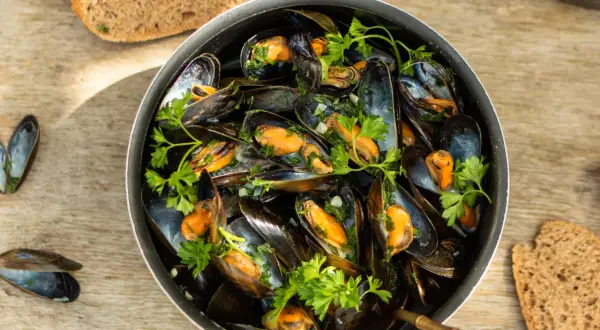 Un plat généreux de moules marinières, garni de persil frais, servi avec du pain de campagne sur une table en bois.