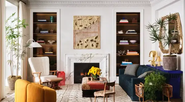 A living room showcasing how to mix modern and vintage decor with a plush yellow armchair, ornate mirror, and a marble fireplace.