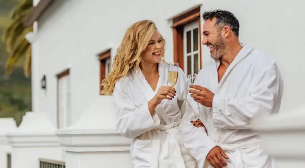 Para, ubrani w szlafroki, wznoszą toasty szampanem na balkonie. Zastanawiają się, ile kosztuje noc w hotelu, ciesząc się luksusem.