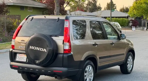 En gyllene Honda CRV 2005 står parkerad på en gata, med reservhjulet synligt på bakluckan.