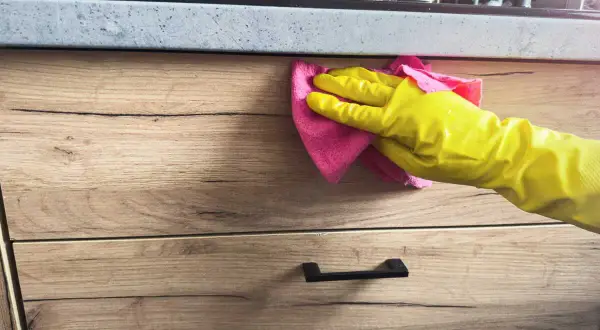 Main jaune essuyant une tache sur bois avec un chiffon rose.