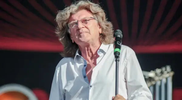 Zbigniew Wodecki śpiewa "Lubię wracać tam, gdzie byłem", z mikrofonem w dłoni, na tle czerwono-czarnej sceny.