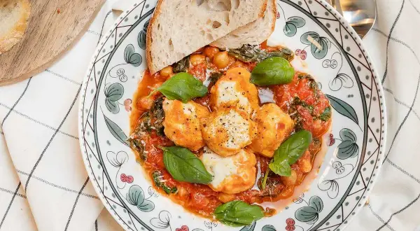 En tallrik med ricotta recept: smakliga ricotta-bollar i tomatsås med kikärtor, spenat och basilika, serverad med rostat bröd.