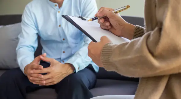 Rozmowa z psychiatrą. Pacjent siedzi na kanapie, lekarz notuje na kartce. Kto to jest psychiatra? To specjalista od zdrowia psychicznego.