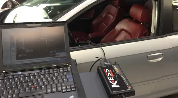 Laptop och KESS-enhet kopplade till en bil för att chippa bilen. Röd läderinredning syns i kupén.