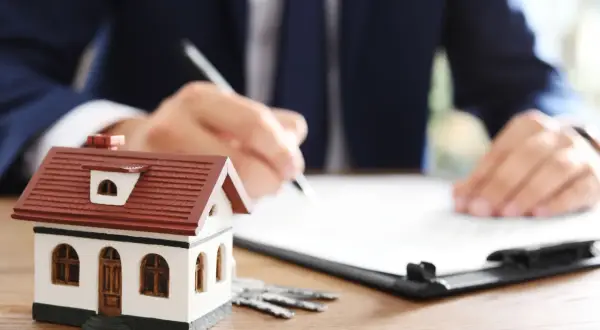 Modellino di casa, chiavi e un uomo che firma un documento. Scopri cos'è la rendita catastale per la tua casa.