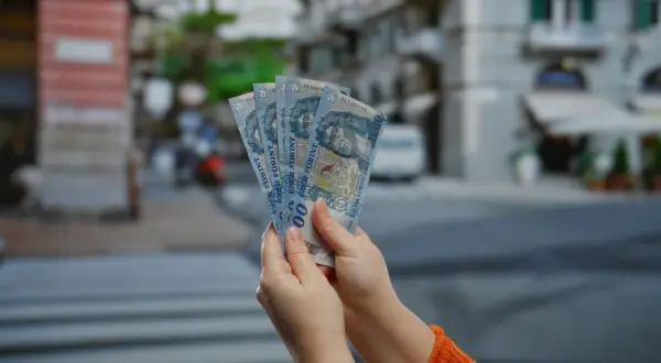 Ręce trzymające banknoty 1000 forintów. W tle widać ulicę, co sugeruje, że chodzi o ceny na Węgrzech.