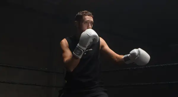 Boxer in white gloves practices a boxing slip in a dark ring, ready for the next round.